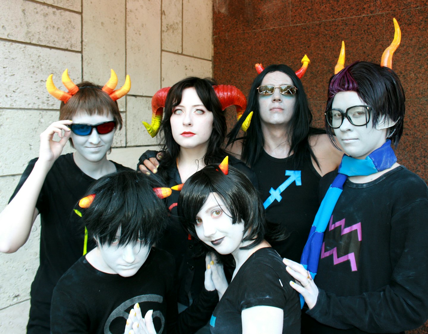 Five cosplayers with striking face paint and horns pose together.