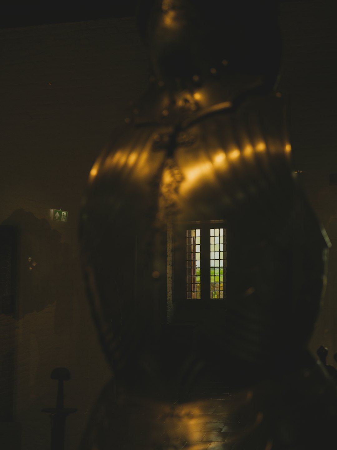 Metallic suit of armor reflecting a green field and exit sign.
