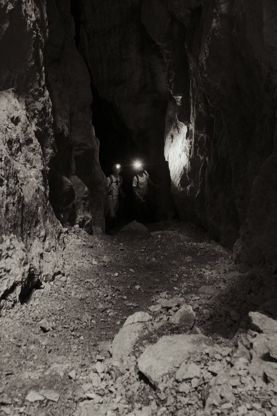 Two explorers with headlamps hike through a dark rocky cave.